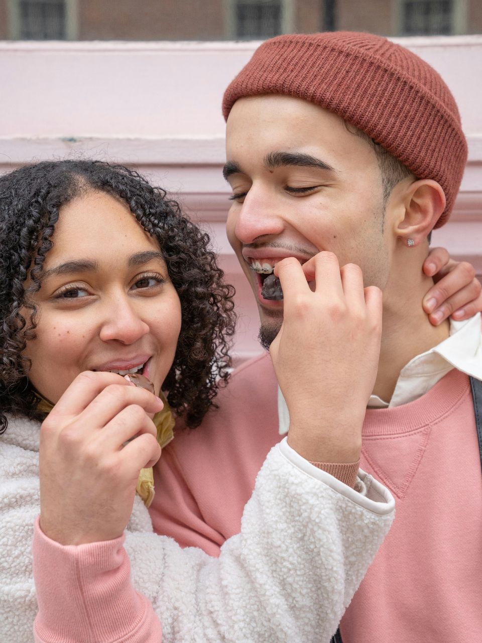 Un couple souriant habillé en rose pâle partageant un moment agréable en mangeant ensemble