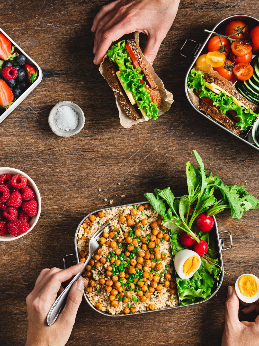 Assortiment de repas sains et un sandwich végétarien, présentés dans des lunch box et Bentos compartimentés en acier inoxydable sur une table en bois