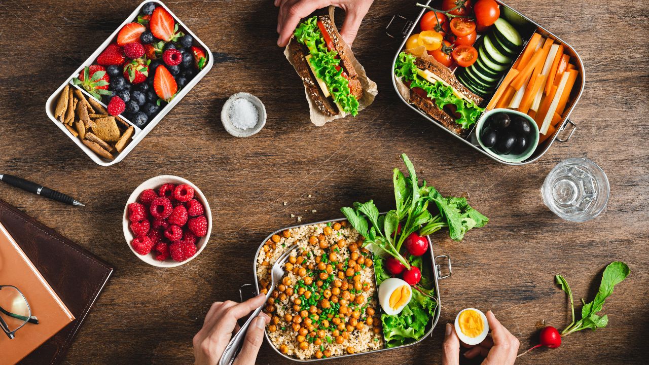 Assortiment de repas sains présentés dans des lunch box compartimentées en acier inoxydable sur une table en bois